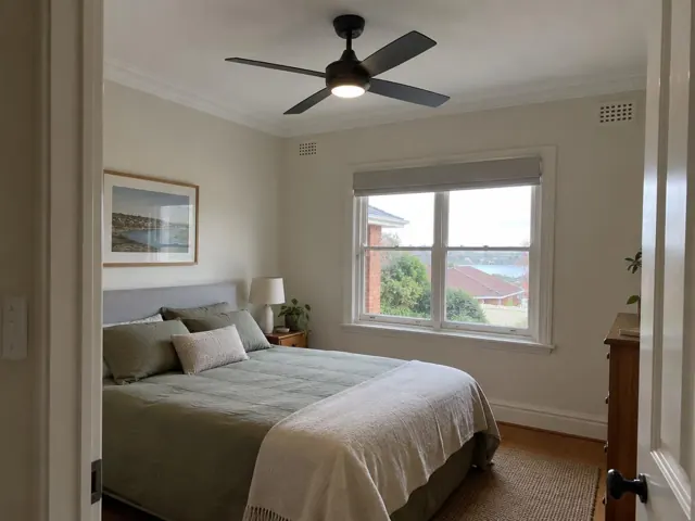 Bedroom with a black ceiling fan, bed, window and bedside table in Boolaroo